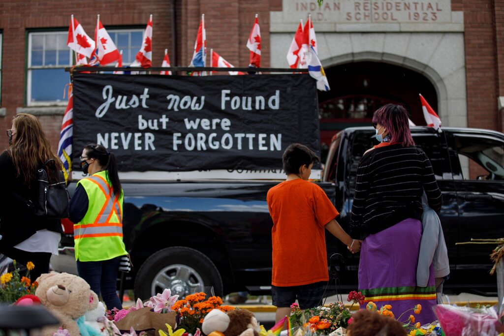 A convoy of vehicles driving past the Kamloops Indian Residential School after the remains of more than 200 children were found buried there in unmarked graves earlier this month.Credit...Cole Burston/Agence France-Presse — Getty Images