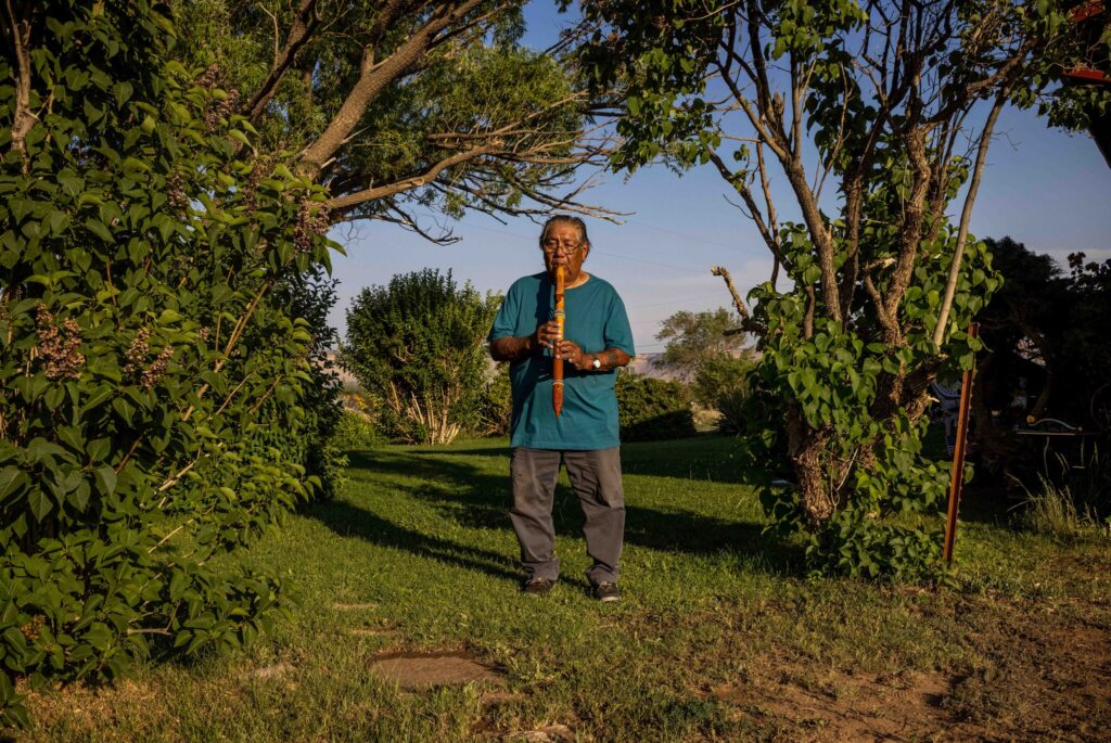 [Norman Lopez, 78, playing a flute outside of his home. He said a boarding school teacher in Colorado smashed his hand-carved flute and threw it in the trash.Credit...Sharon Chischilly for The New York Times]