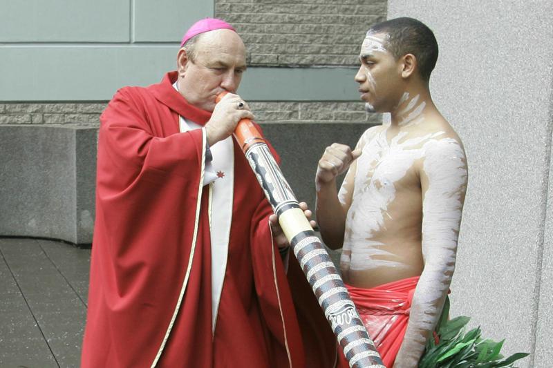 FILE - In this April 17, 2008 file photo, Bishop Christopher Saunders of Broome tries to play a digeridoo during a World Youth day 2008 media event in Sydney, Australia. Pope Francis has replaced Bishop Christopher Saunders, who stepped down amid a Vatican investigation into what Australian media have described as allegations of sexual misconduct. (AP Photo/Rob Griffith)