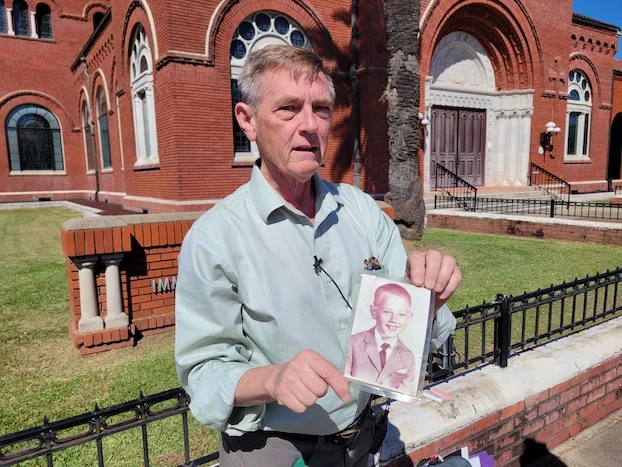 David Clohessy holds a photo of himself at a much younger age as he stands in front of Immaculate Conception in Lake Charles to talk about clergy abuse. (Rita LeBleu / American Press)  Read more at: https://www.americanpress.com/2024/10/08/clergy-abuse-victim-four-more-local-priests-should-be-on-credibly-accused-list/