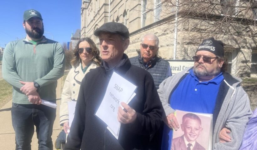 SNAP Missouri Director David Clohessy, middle front, speaks outside of the Spalding Pastoral Center in downtown Peoria. He's surrounded by victims of child sex abuse and their families, who asked not to be identified by name. Some carry photos of children at the age when they were abused. Collin Schopp